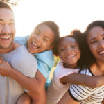 Family of four in their yard facing the camera smiling