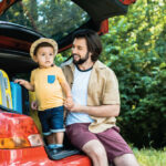 Father and sun sitting in the back of their car trunk